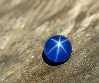 High-resolution close-up of a natural blue star sapphire displaying a sharp six-ray star under sunlight, placed on a textured wooden surface.