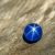 High-resolution close-up of a natural blue star sapphire displaying a sharp six-ray star under sunlight, placed on a textured wooden surface.