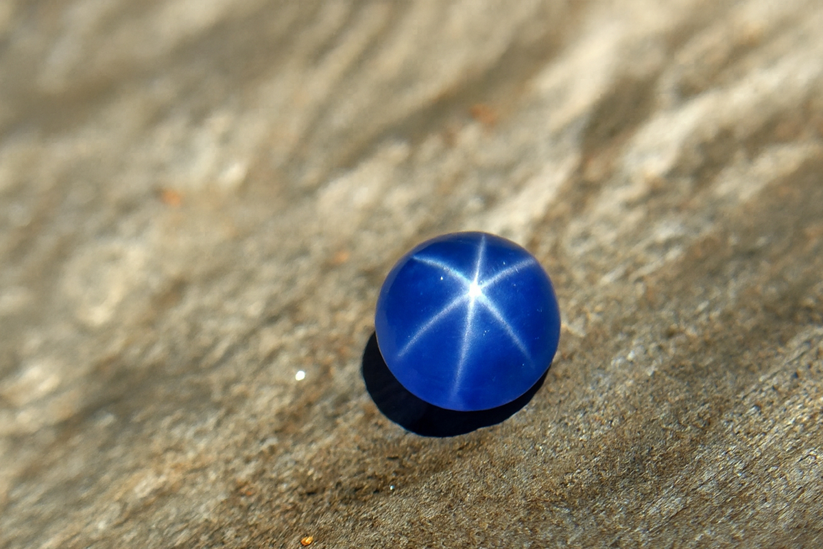 High-resolution close-up of a natural blue star sapphire displaying a sharp six-ray star under sunlight, placed on a textured wooden surface.